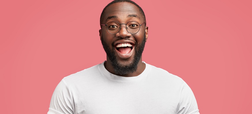 a black man wearing glasses smiling in front of a pink backdrop