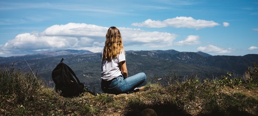 a girl sitting high on a mountain overlooking the sky