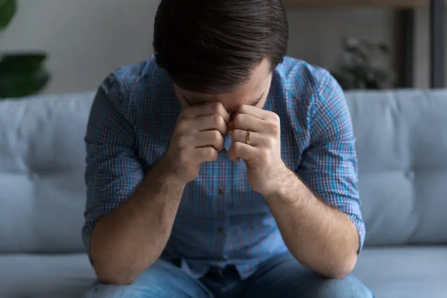 man sitting on couch suffering from stress depression and headaches