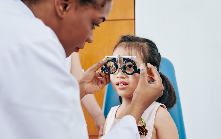optometrist helping little girl to put on test glasses when checking her eyesight