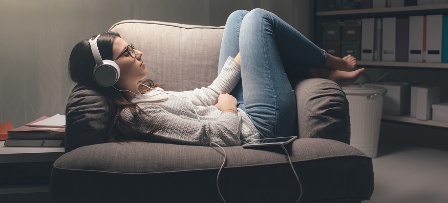 a female laying on an arm chair listening to music through headphones