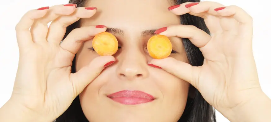 woman holding carrot slices over eyes