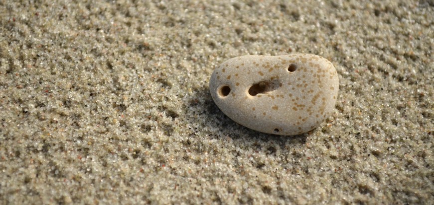 Pebble on the sand with holes forming a face